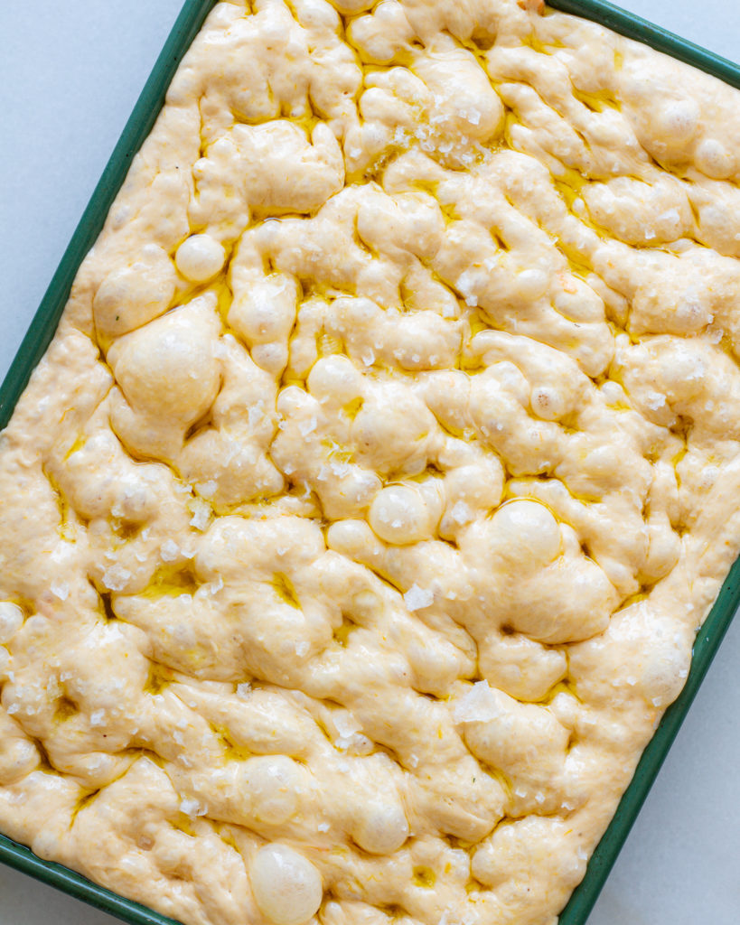 dimpled focaccia dough on baking sheet with olive oil and salt