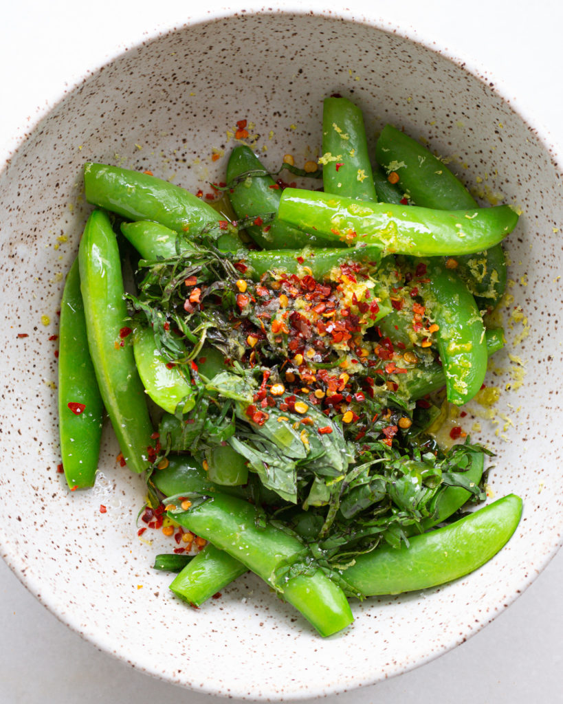 Snap peas in bowl with lemon zest, herbs, and seasoning