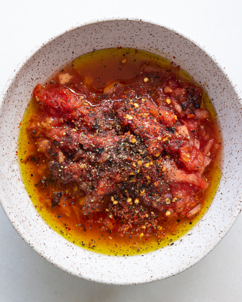 Chopped blistered tomatoes with seasonings and olive oil in bowl