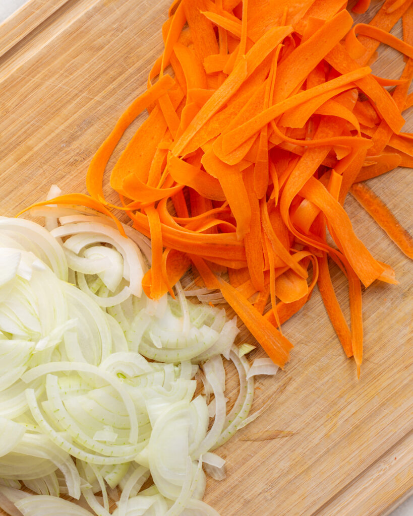 Peeled carrots and sliced onions on a cutting board