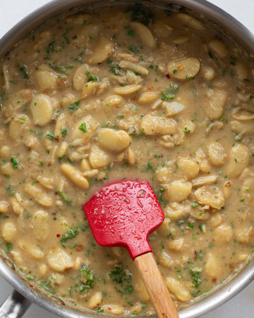 garlic butter beans in a pan being stirred with a red spatula