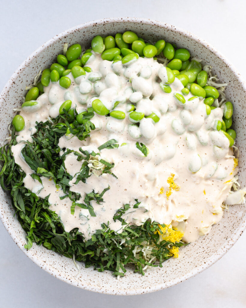 Ingredients for cabbage salad layered in a mixing bowl, with the charred lemon dressing poured on top
