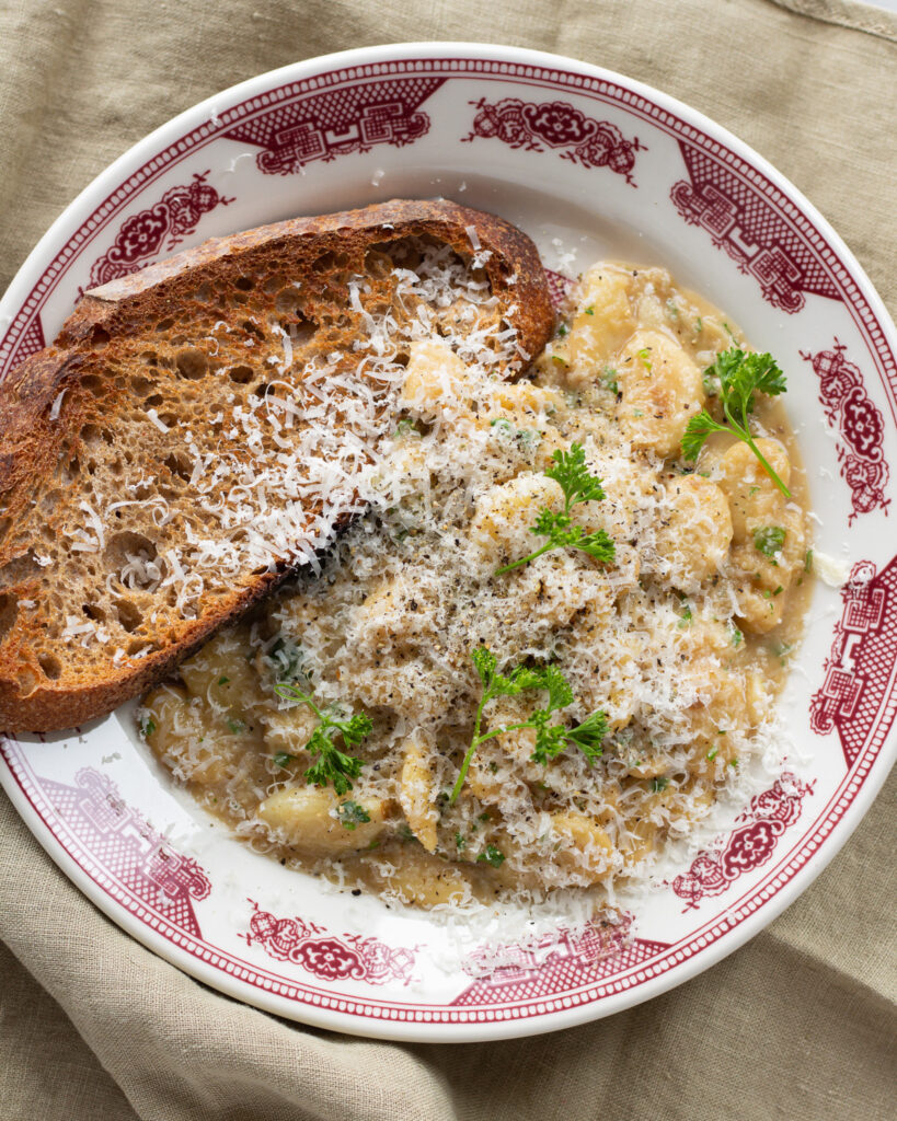 A plate of garlic butter beans with toasted bread, topped with shaved parmesan cheese and parsley