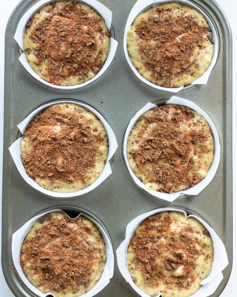 Zucchini muffin batter in muffin tin topped with cinnamon chocolate