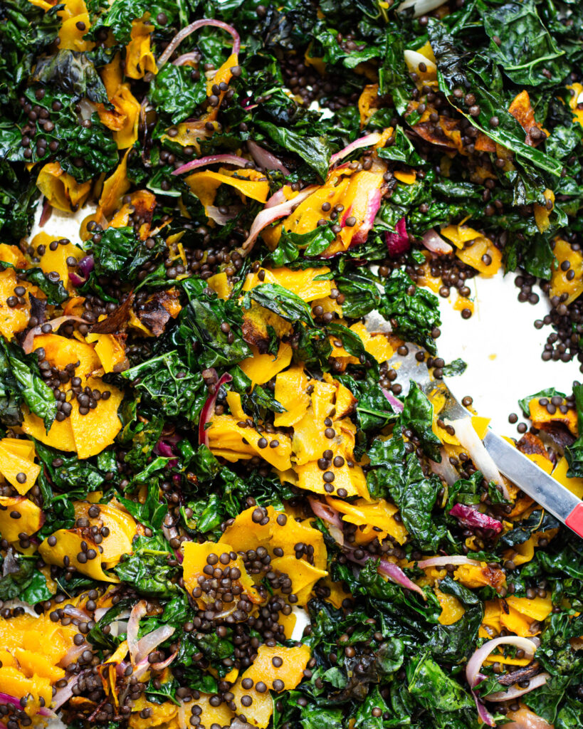 Butternut squash, lentils, red onion, and kale tossed together on a sheet tray