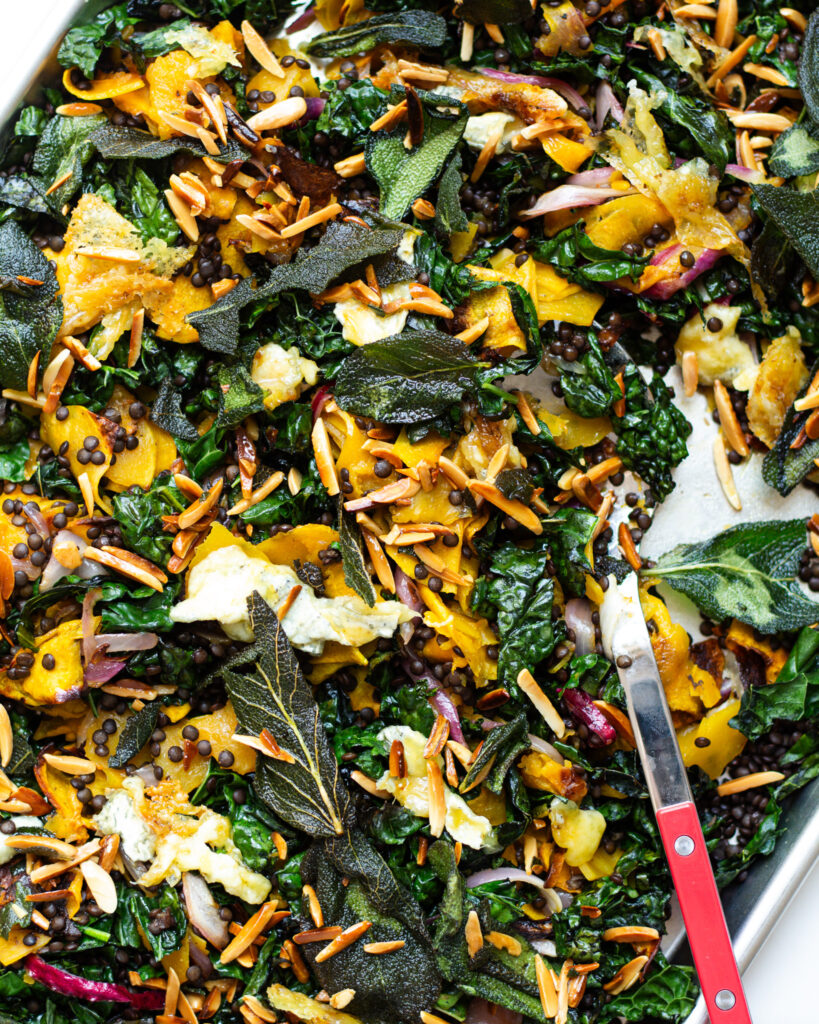 Ingredients tossed together on a sheet tray for a baked kale salad with apple cider vinaigrette and griddled goat cheese