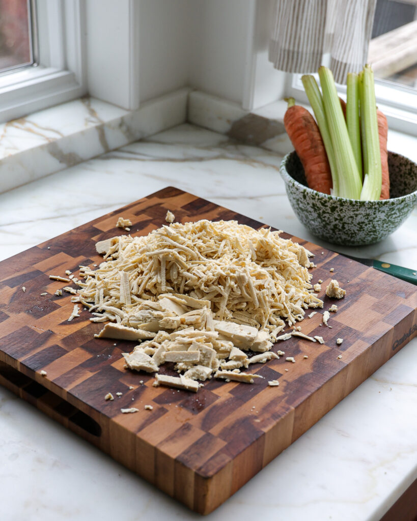 Shredded tofu on a cutting board getting prepped for a vegetarian chicken noodle soup 