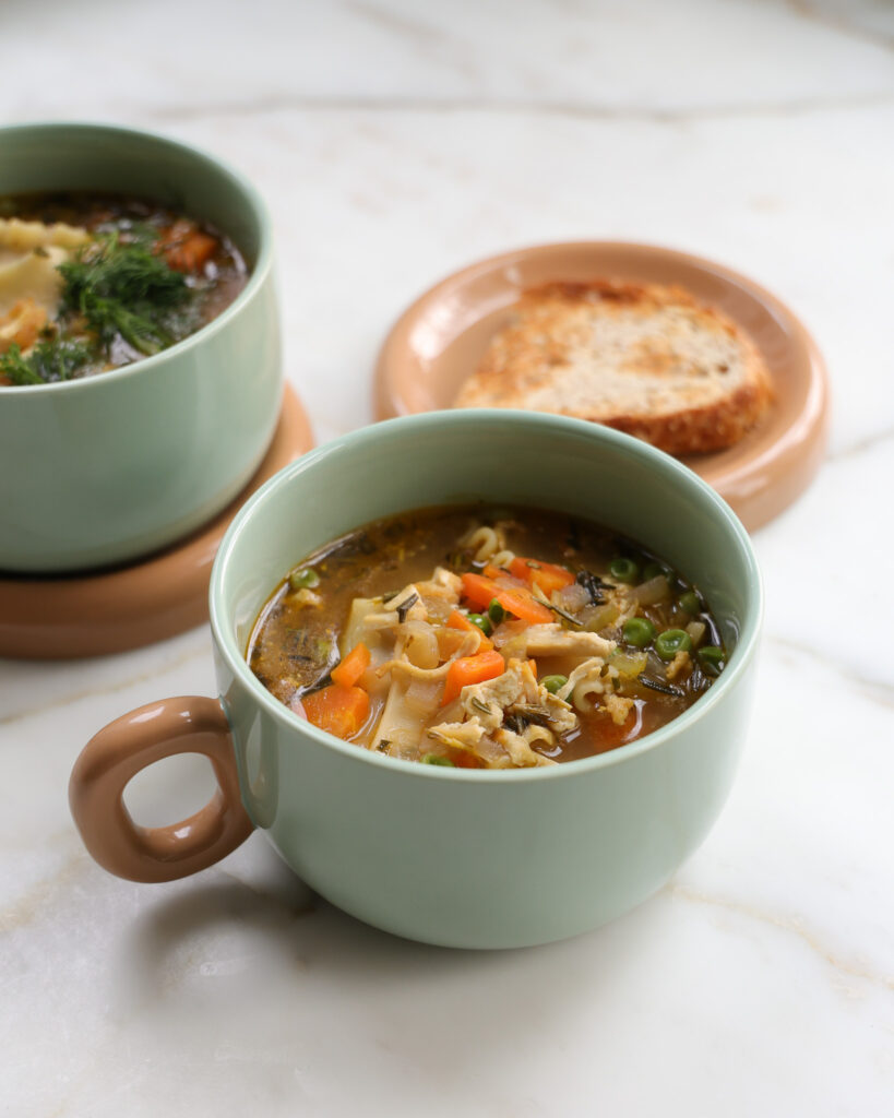 Two bowls of vegetarian noodle soup with a side of bread