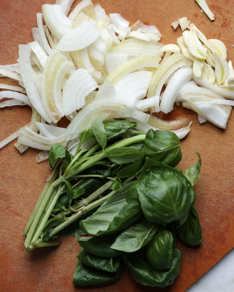 basil and sliced onion on a cutting board.