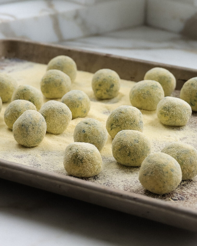 Pumpkin ricotta gnudi on a baking sheet sprinkled with semolina flour.