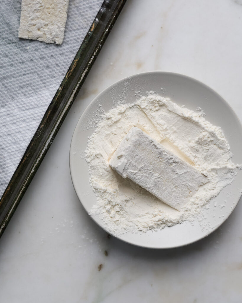 Tofu slices being tossed in flour.