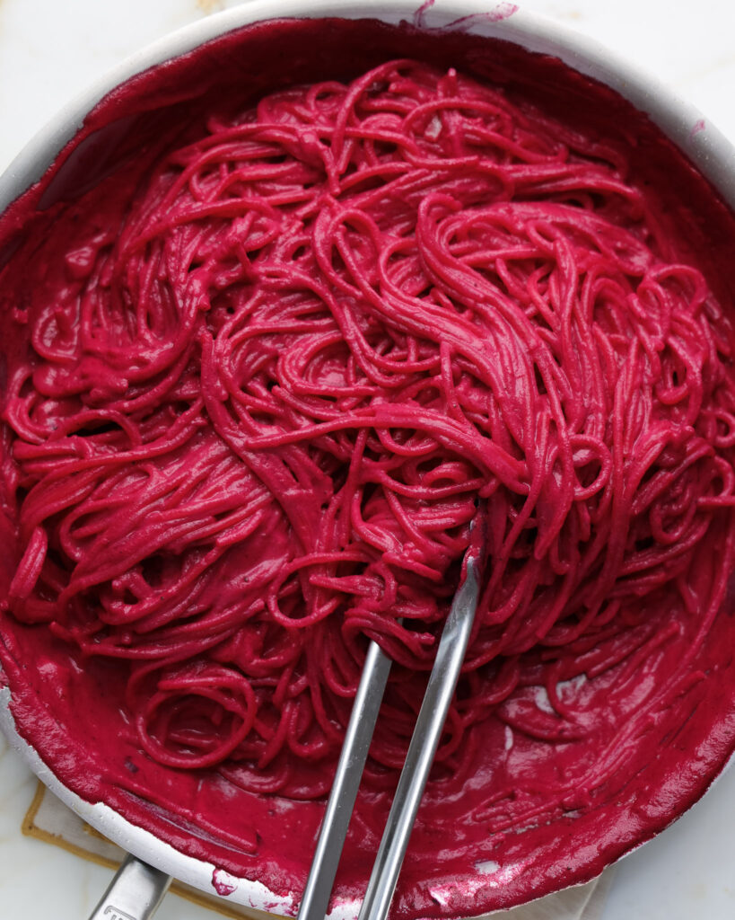 Pasta being tossed in a beet sauce.
