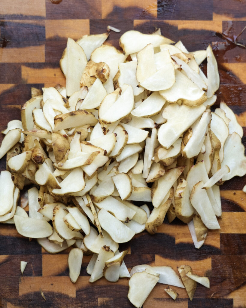Thinly sliced sunchokes on a cutting board.