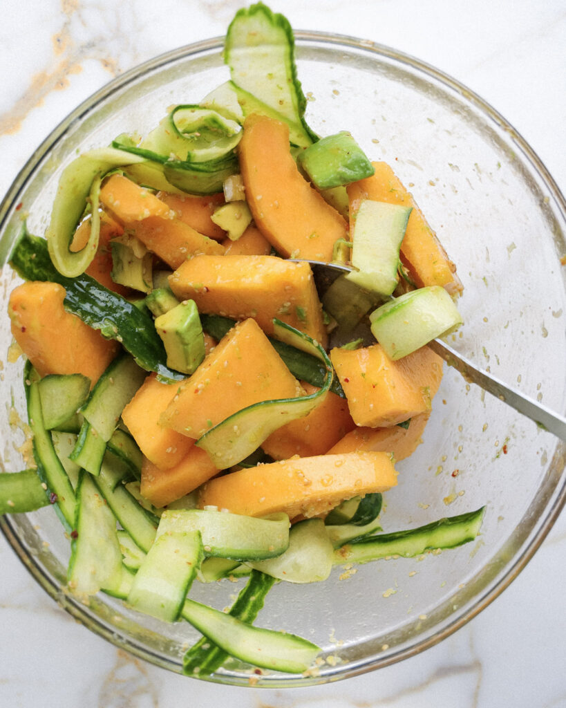 cucumber, melon, lime zest and avocado being tossed in a bowl.