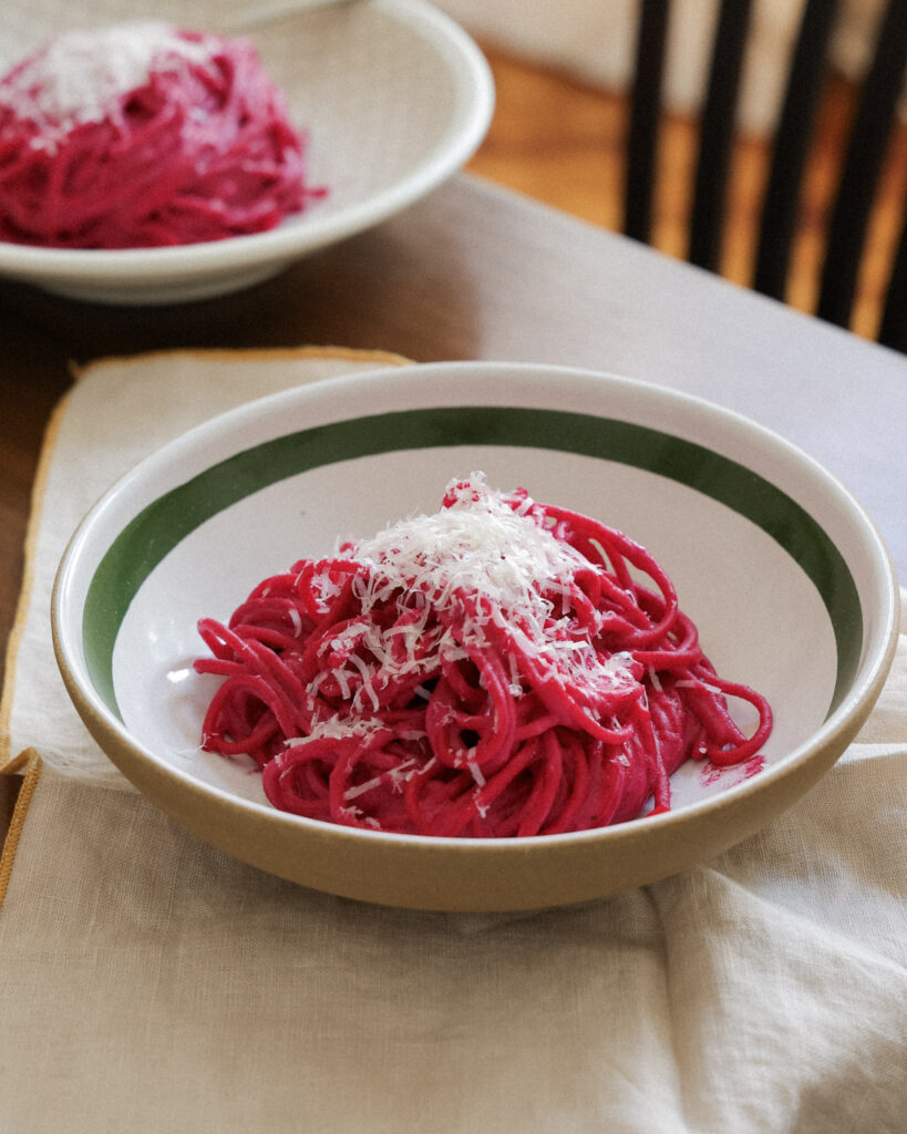 Beet pasta in a bowl topped with parmesan.