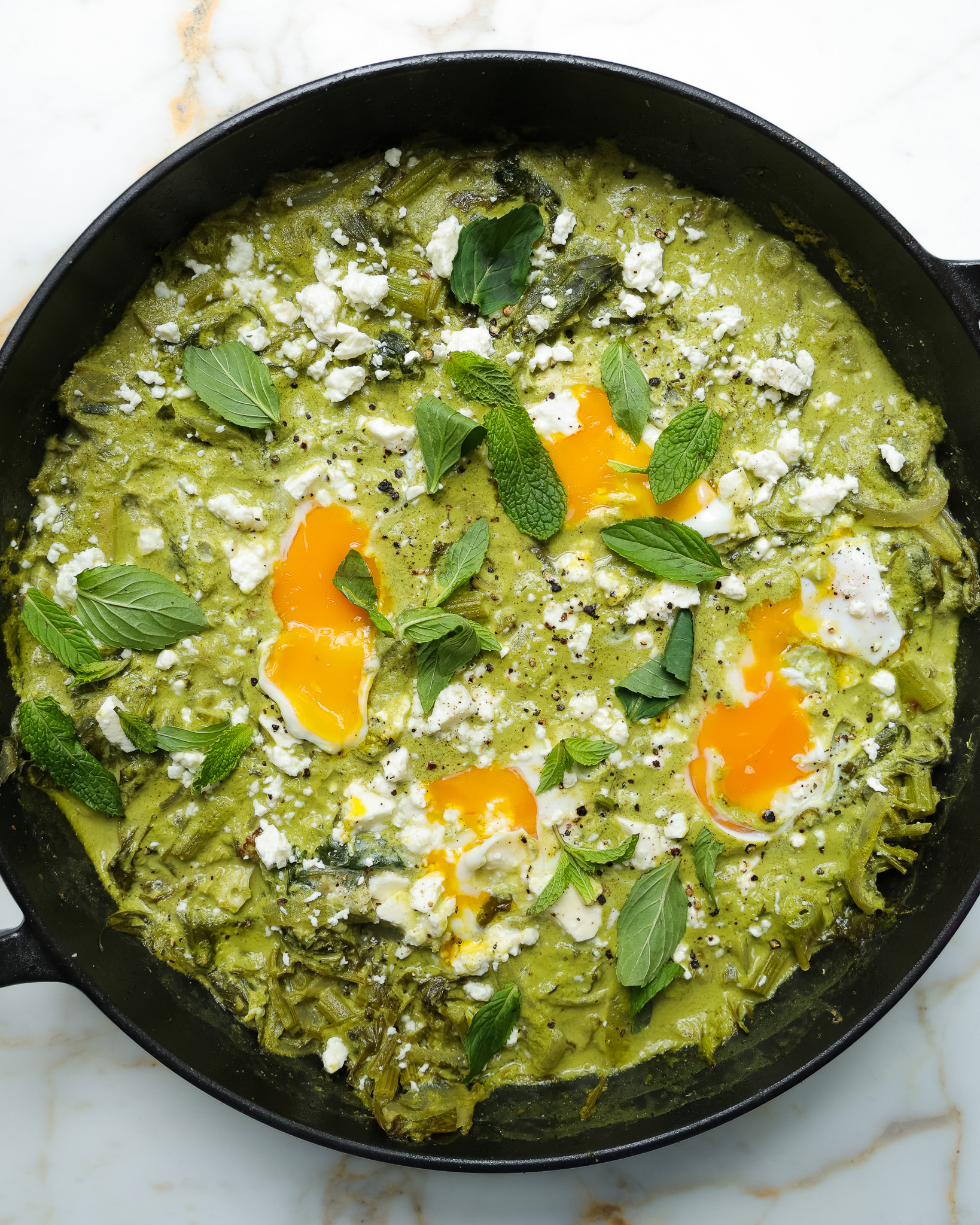 spring green shakshuka in a cast iron skillet topped with mint.